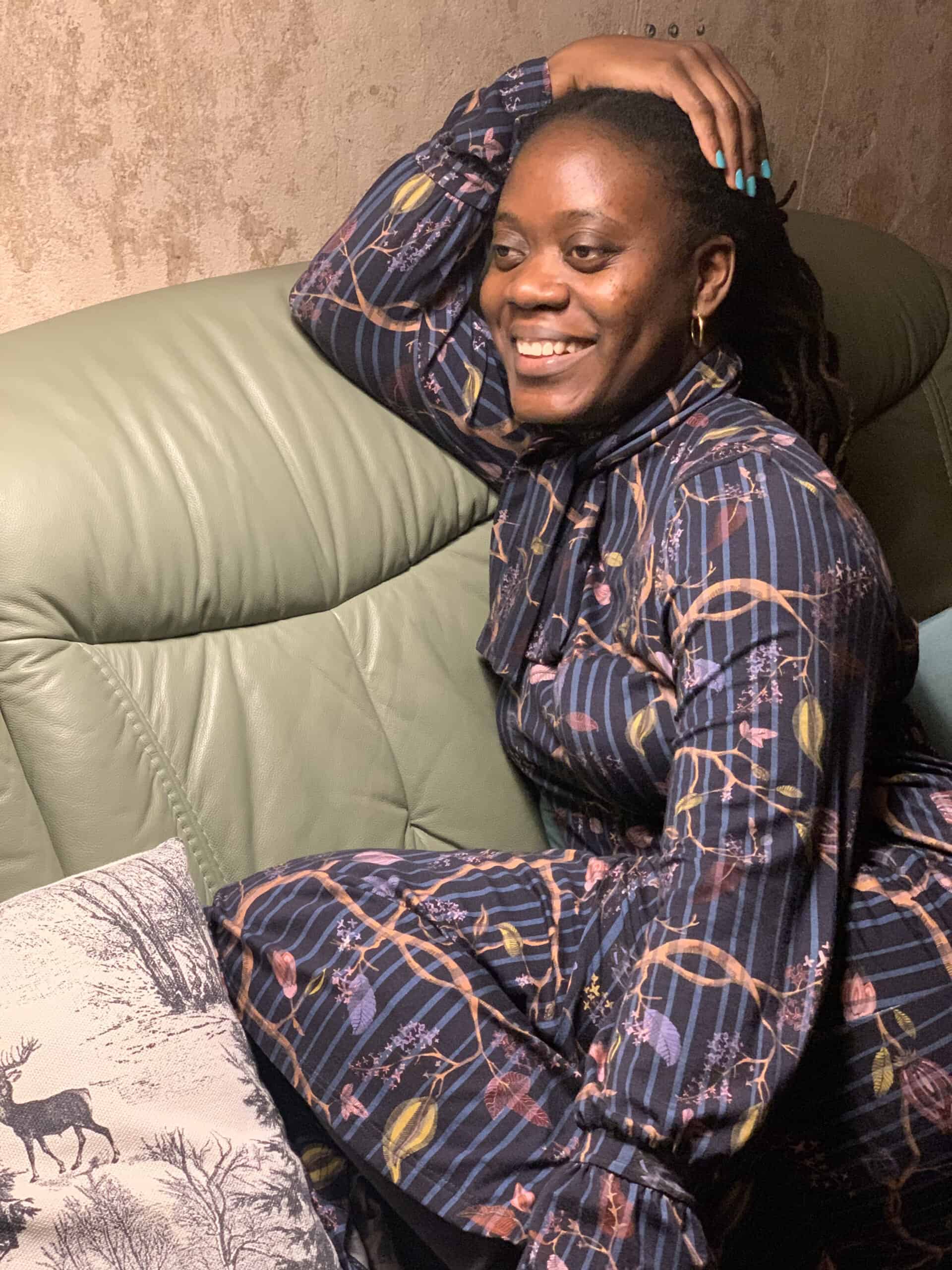 Smiling woman with dreadlocks relaxing on a sofa in stylish pajamas.